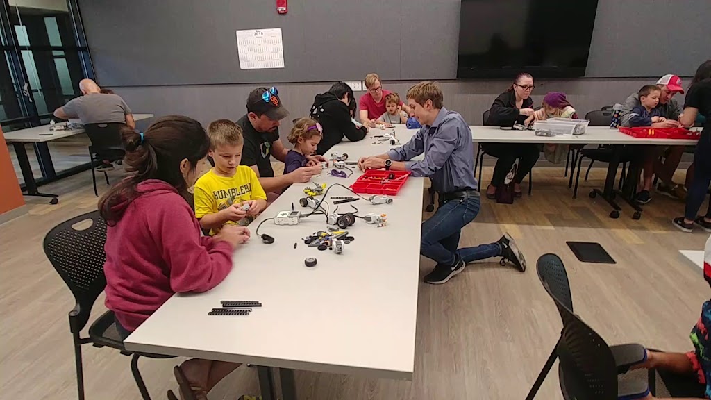 Demonstration of class being run by a teacher, while parents are helping their kids build simple machine.